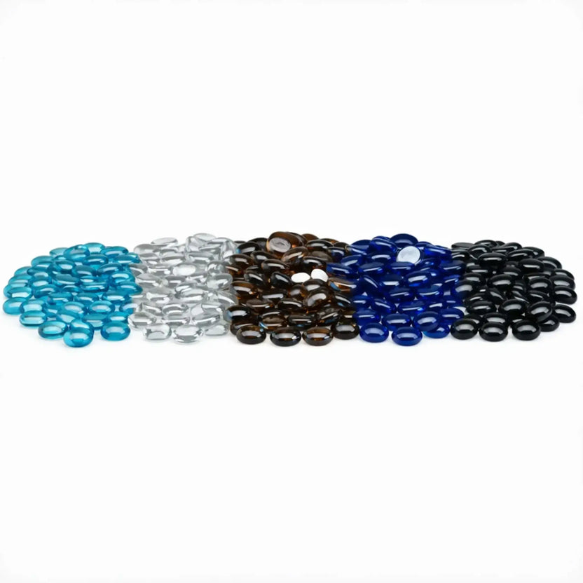 Assorted tempered glass fire pit beads arranged in neat rows by color, featuring aqua blue, glacier ice clear, root beer brown, royal blue, and twilight black luster drops with smooth rounded shapes and a glossy, reflective finish on a white background.