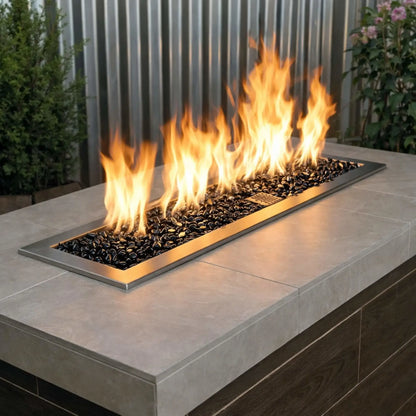 Contemporary outdoor fire table with a linear stainless steel burner filled with twilight black tempered glass beads, accented by bright yellow flames in a modern patio setting.