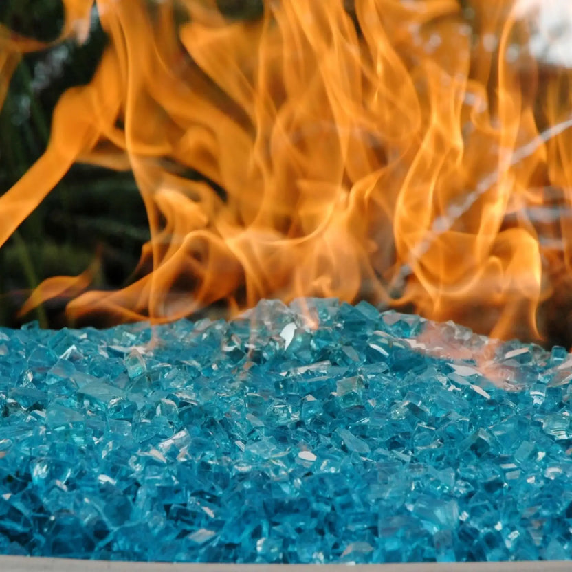Close-up view of half-inch classic non-reflective Azuria fire glass showcasing rich turquoise-blue tempered glass pieces with smooth, angular edges as vivid orange flames curl and dance just above the surface, highlighting the depth of color and texture in a modern outdoor gas fire feature.