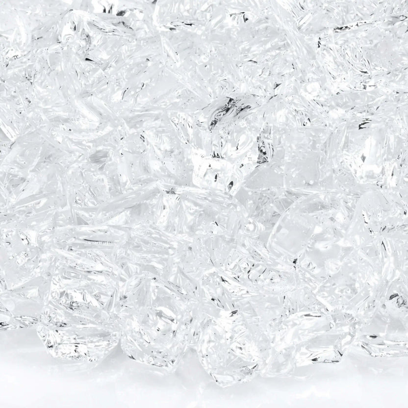 Macro close-up of 1/2 inch non-reflective Starfire Ultra Clear tempered fire glass pieces, showing brilliant clarity, subtle internal texture, and smooth tumbled surfaces that allow natural gas flames to shine through with bright, crisp illumination.