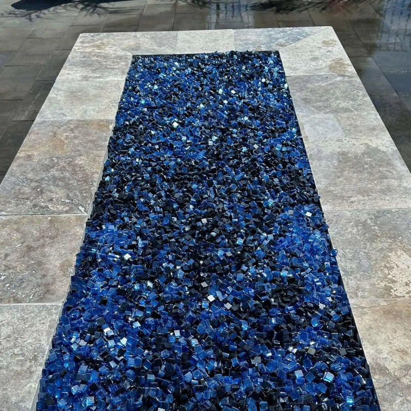 Rectangular fire pit insert showcasing a blend of black and Pacific blue Luster 2.0 tempered fire glass cubes, arranged in a tiled stone surround. The rich blue tones contrast with the darker cubes, creating a bold, eye-catching fire bed designed for contemporary outdoor fire features.