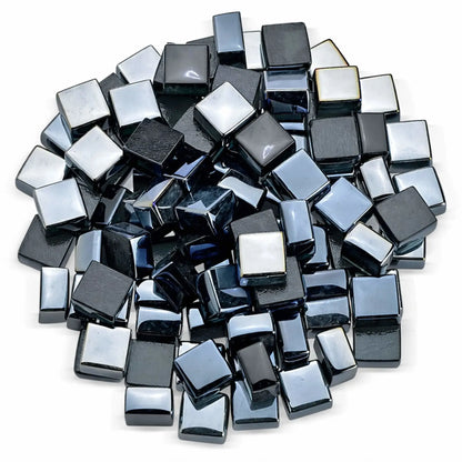 Top-down studio view of black Luster 2.0 half-inch tempered fire glass cubes arranged in a loose circular pile on a white background. The polished, mirror-like surfaces and beveled edges highlight the depth and reflective quality ideal for gas fireplaces and fire pits.