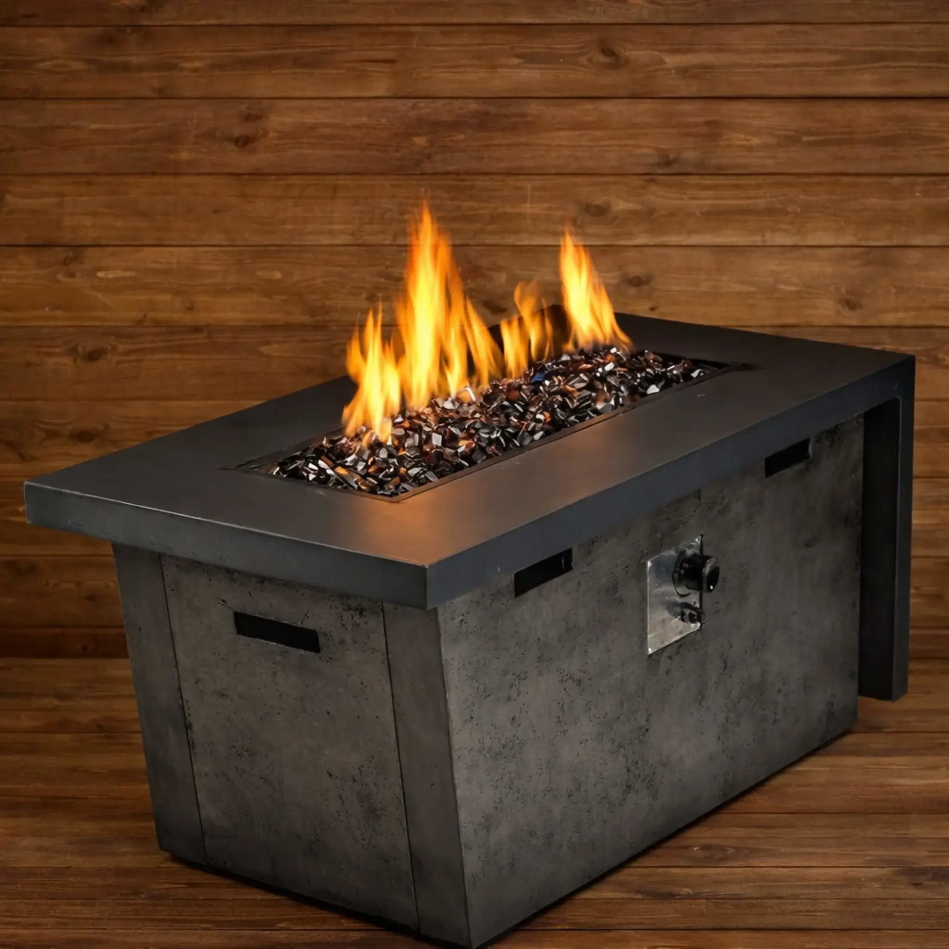 Modern rectangular gas fire table filled with copper Luster 2.0 half-inch fire glass cubes, producing tall, bright flames against a warm wood plank backdrop. The glowing amber glass reflects the firelight, creating a cozy yet contemporary patio focal point.