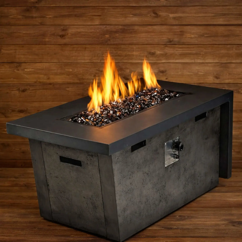 Modern rectangular gas fire table filled with copper Luster 2.0 half-inch fire glass cubes, producing tall, bright flames against a warm wood plank backdrop. The glowing amber glass reflects the firelight, creating a cozy yet contemporary patio focal point.