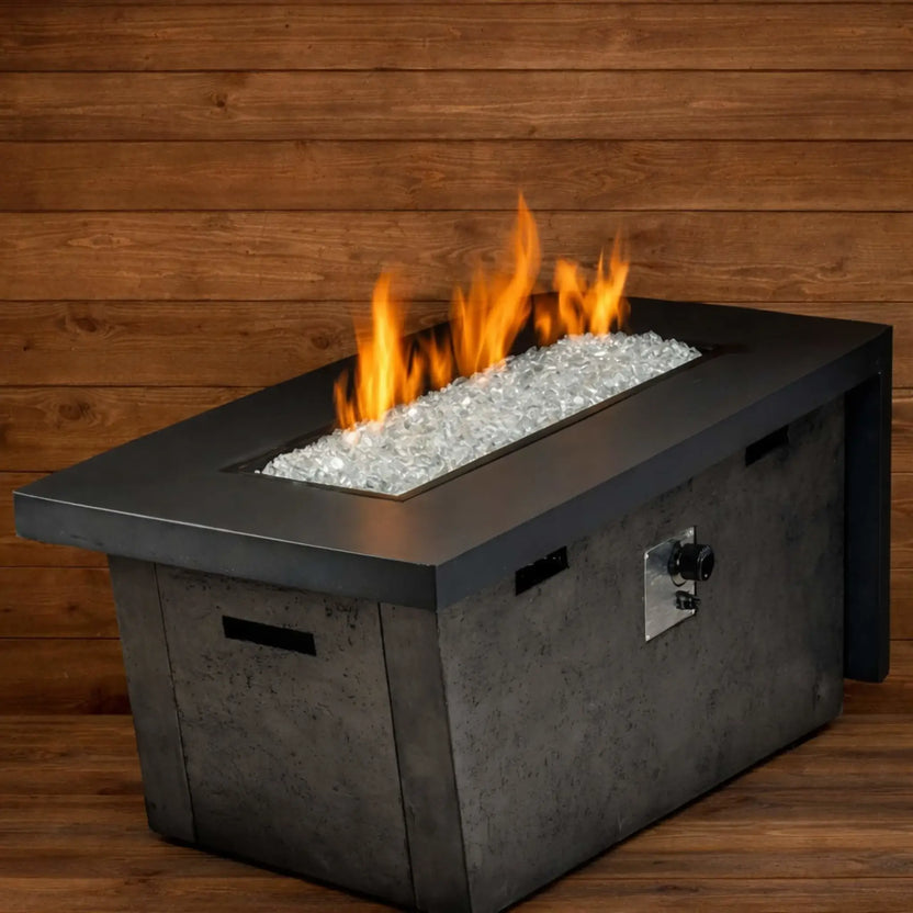Rectangular modern gas fire table filled with Starfire clear white Luster 2.0 tempered fire glass cubes, producing warm orange flames against a wood-paneled backdrop. The light, crystalline glass enhances the brightness of the fire for a clean, contemporary outdoor look.