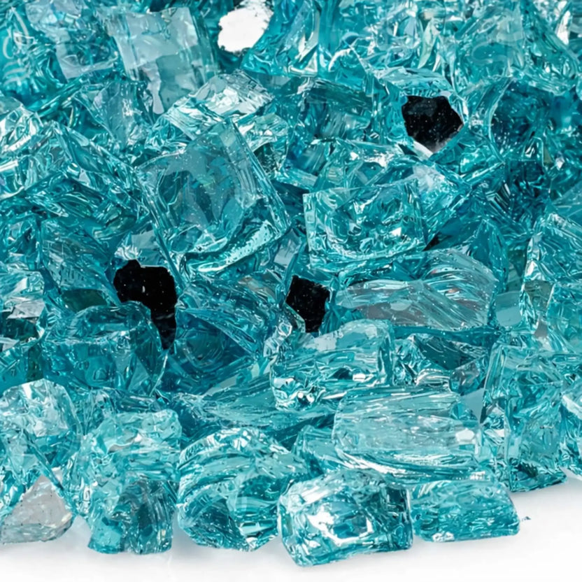 Close-up macro view of 1/2 inch reflective Azuria tempered fire glass from American Fire Products, highlighting the translucent aqua blue color, sharp faceted edges, smooth polished surfaces, and reflective backing that enhances light and flame brilliance.