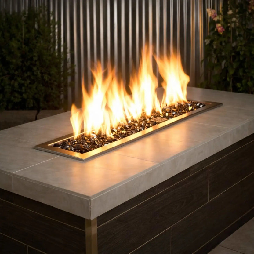 Contemporary linear outdoor fire pit burner filled with American Fire Products 1/2 inch premium reflective black fire glass, producing bright golden flames across a sleek rectangular stainless steel insert in a modern patio setting.
