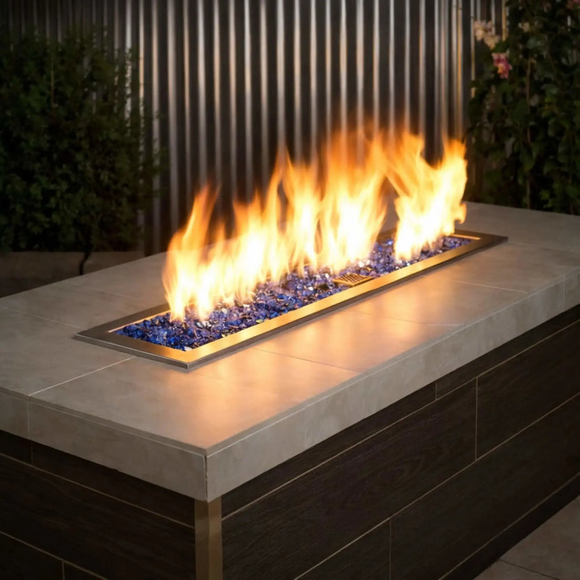 Contemporary rectangular fire pit table featuring American Fire Products 1/2 inch premium reflective cobalt blue fire glass, glowing beneath bright yellow flames in a stainless steel burner pan set into a modern outdoor patio setting.