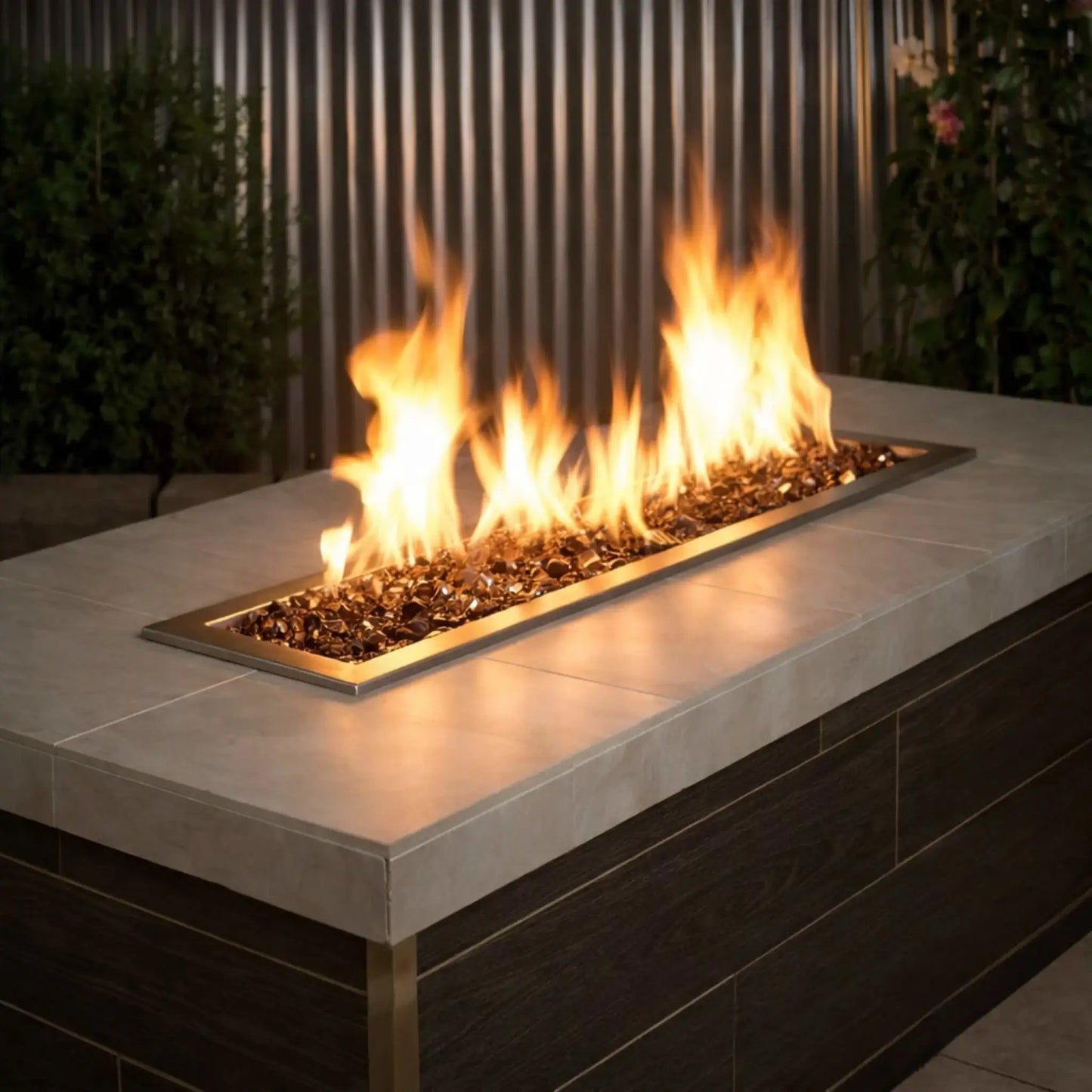 Modern linear outdoor gas fire pit filled with American Fire Products 1/2 inch premium reflective copper fire glass, featuring vibrant yellow flames dancing across a sleek stainless steel burner in a contemporary patio environment.