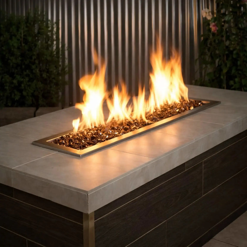 Modern linear outdoor gas fire pit filled with American Fire Products 1/2 inch premium reflective copper fire glass, featuring vibrant yellow flames dancing across a sleek stainless steel burner in a contemporary patio environment.
