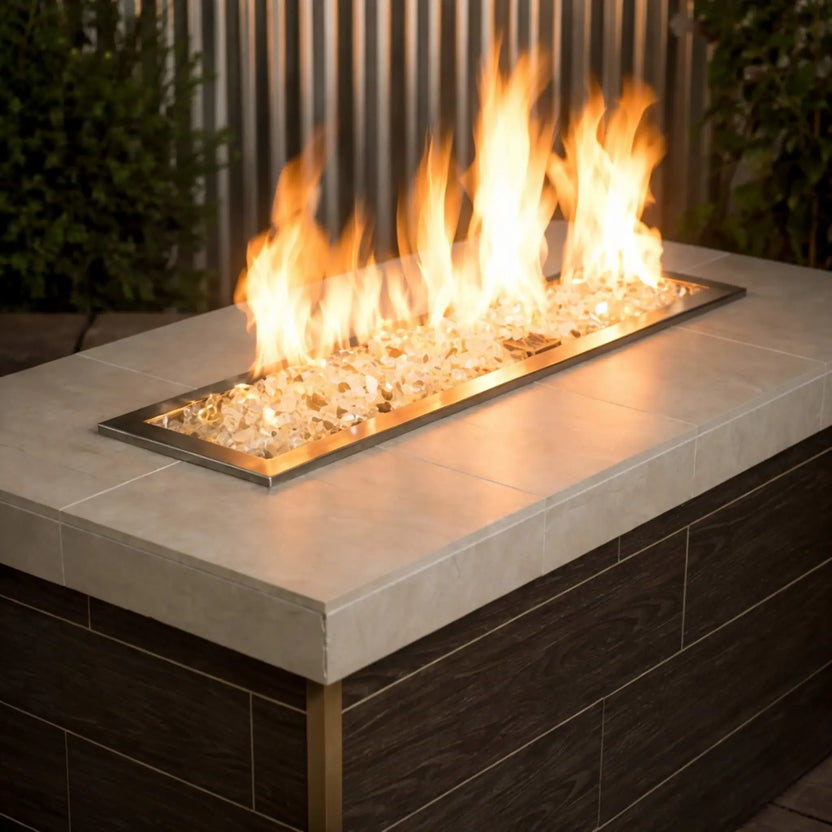 Contemporary rectangular fire pit table filled with American Fire Products 1/2 inch premium reflective gold fire glass, where bright yellow flames dance across a stainless steel burner pan in a modern outdoor patio setting.