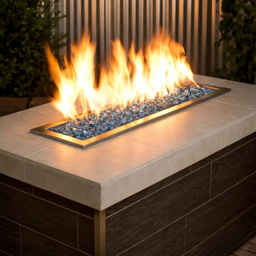 Contemporary rectangular gas fire pit filled with American Fire Products 1/2 inch premium reflective Pacific blue fire glass, where bright yellow flames dance across a stainless steel burner pan set into a modern patio fire table.