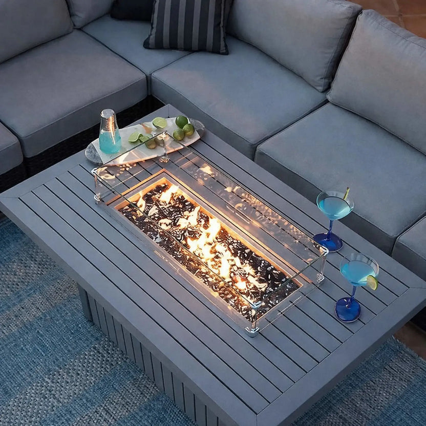Contemporary outdoor sectional seating area featuring a rectangular fire table with black glass beads under bright flames, accented by blue cocktails and lime garnish on the tabletop.