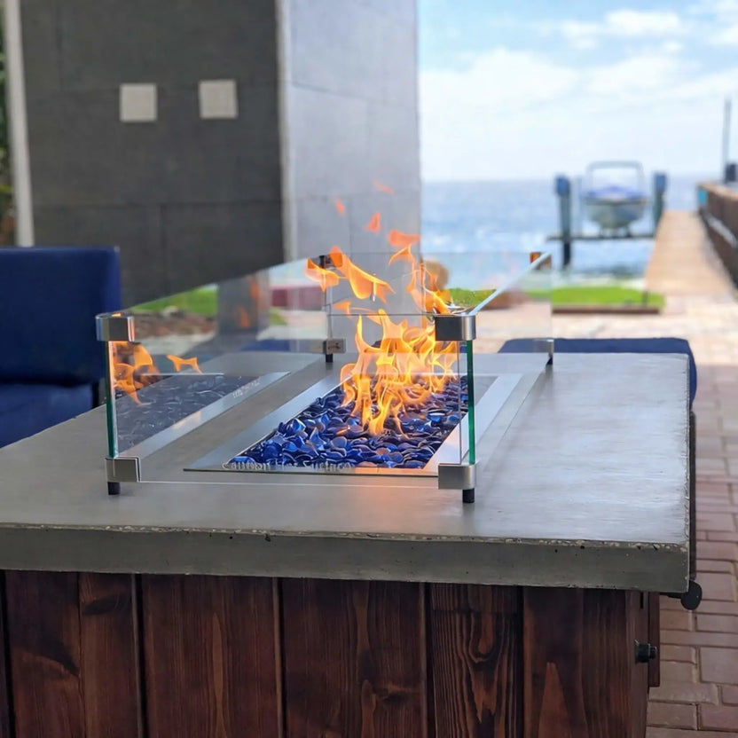 Contemporary linear fire feature built into a stone bench, glowing with bright flames over deep blue tempered glass beads in a landscaped backyard with tiered rock retaining walls.