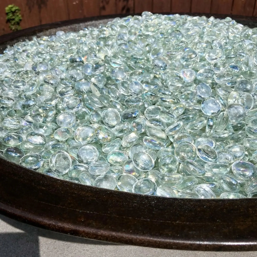 Round fire bowl fully filled with clear tempered glass luster beads, their polished surfaces catching the light and creating a soft, crystal-like shimmer.