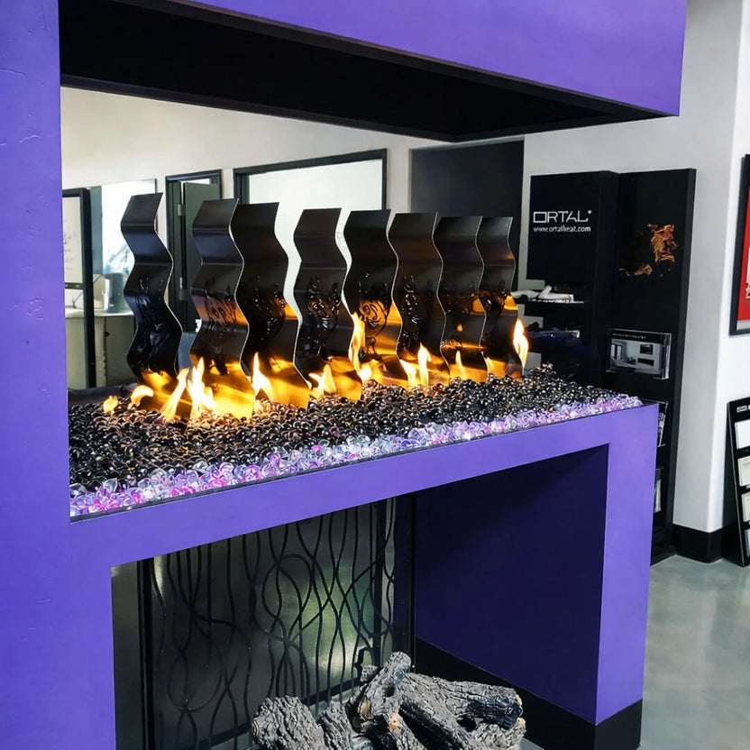 Modern showroom fireplace display with black glass beads and decorative metal flame dividers, framed in a bold purple surround with visible flames rising above the media.