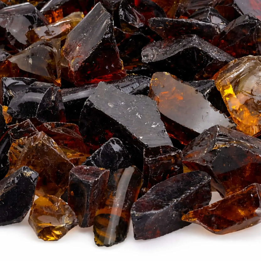Close-up detail of Auburn tempered fire glass showing jagged, polished edges and layered tones of honey, caramel, and dark espresso brown with light reflecting through the translucent shards.
