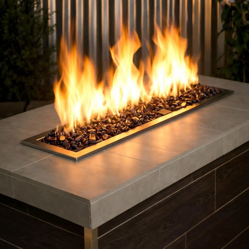 Modern rectangular outdoor fire feature filled with dark blue tempered fire glass, with bright yellow flames rising above a sleek concrete tabletop in a contemporary patio setting.