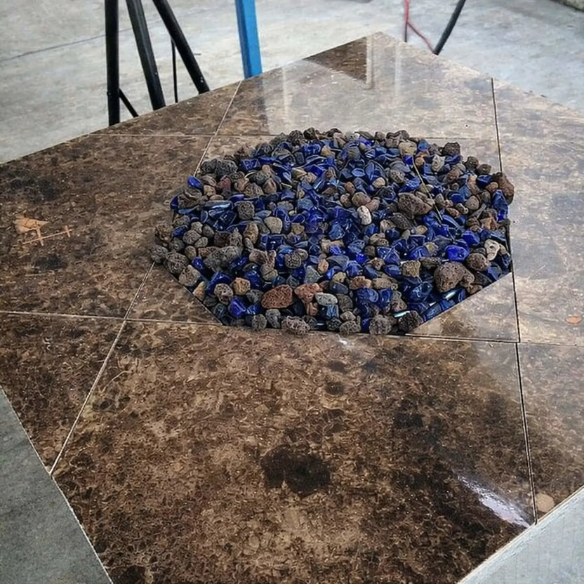 Hexagon fire pit table with a brown stone top filled with dark blue tempered fire glass and lava rock base, creating a striking centerpiece for an outdoor patio space.