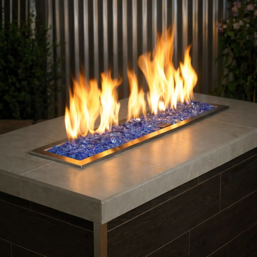 Modern rectangular fire table filled with light blue tempered fire glass, with bright yellow flames rising above a stainless steel burner set into a concrete tabletop.