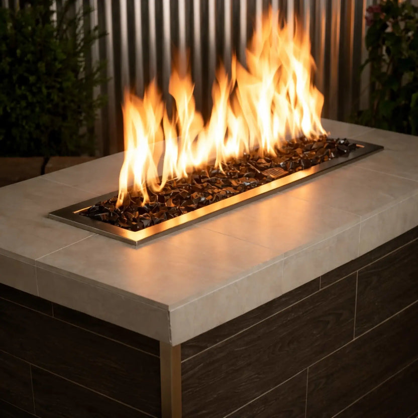 Modern linear gas fire table filled with Onyx Black fire glass, with tall golden flames rising from a stainless steel burner set into a sleek concrete tabletop.