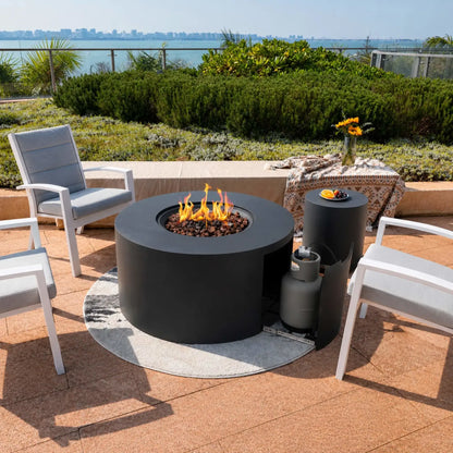 The Elementi Art of Living Pacaya Dark Grey hidden propane fire pit table is shown in operation with bright flames rising above natural lava rock media. An open side access panel reveals the concealed propane tank and hidden drawer storage system, demonstrating easy fuel access while maintaining the fire table’s clean circular design. Modern patio seating surrounds the outdoor fire feature.