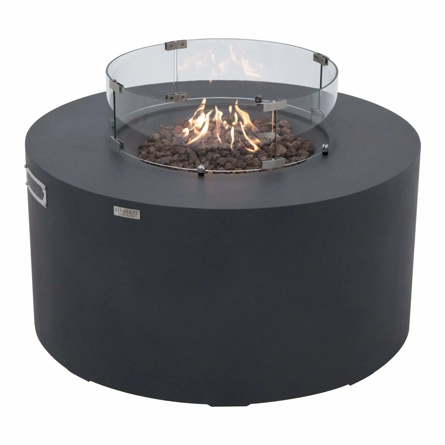 Three-quarter angle view of the Elementi Art of Living Pacaya Dark Grey round GFRC concrete fire pit table operating with visible flames inside the recessed fire bowl. The tempered glass wind guard surrounds the lava rock burner area, highlighting the hidden propane functionality and contemporary outdoor fire feature design.