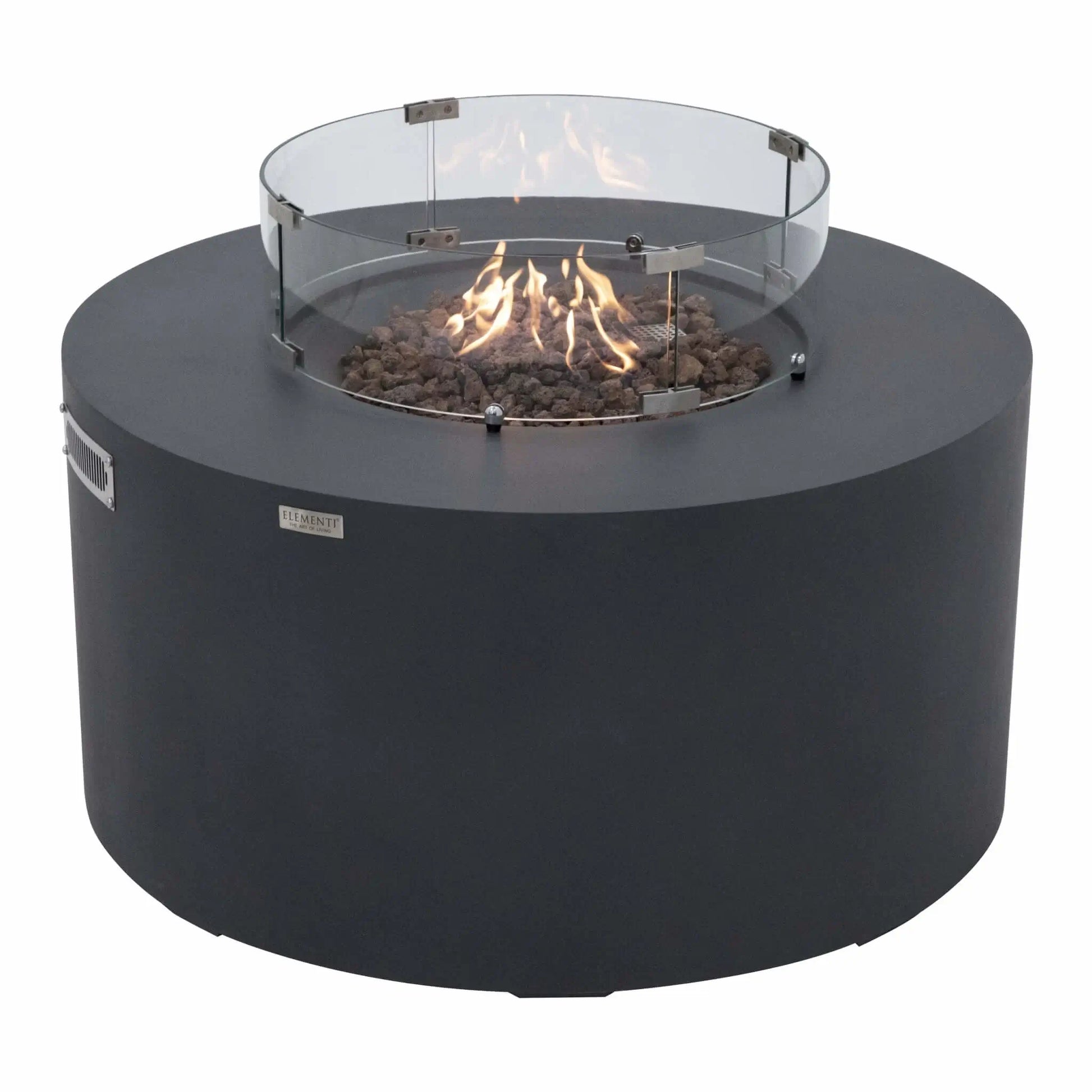 Three-quarter angle view of the Elementi Art of Living Pacaya Dark Grey round GFRC concrete fire pit table operating with visible flames inside the recessed fire bowl. The tempered glass wind guard surrounds the lava rock burner area, highlighting the hidden propane functionality and contemporary outdoor fire feature design.