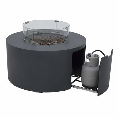 Product image of the Elementi Art of Living Pacaya Dark Grey round GFRC concrete fire pit table with the hidden propane drawer extended. The sliding compartment reveals the concealed propane tank storage system beneath the fire bowl, while the tempered glass wind guard and lava rock media remain installed above.