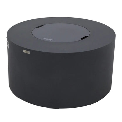 Angled perspective of the Elementi Art of Living Pacaya Dark Grey round fire pit table with the burner cover installed. The GFRC concrete fire pit table showcases its circular profile, hidden propane configuration, recessed lid handles, smooth dark grey finish, and modern outdoor design, photographed on a white background to highlight construction details and overall shape.