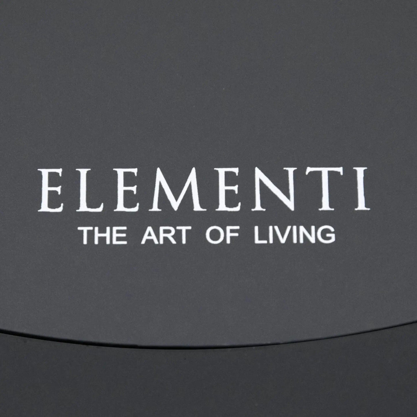 Close-up of the Elementi Art of Living branding printed on the removable burner cover of the Pacaya Dark Grey round fire pit table. The image showcases the clean finish of the GFRC concrete surface and reinforces the premium design details associated with this hidden propane outdoor fire feature.