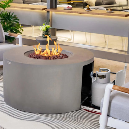 Elementi Art of Living Pacaya Light Grey round fire pit table operating with vibrant flames rising from the lava rock burner bed while the hidden propane drawer is extended. The concealed propane tank storage system is visible beside the outdoor seating arrangement, demonstrating both the fire feature performance and integrated hidden propane design.