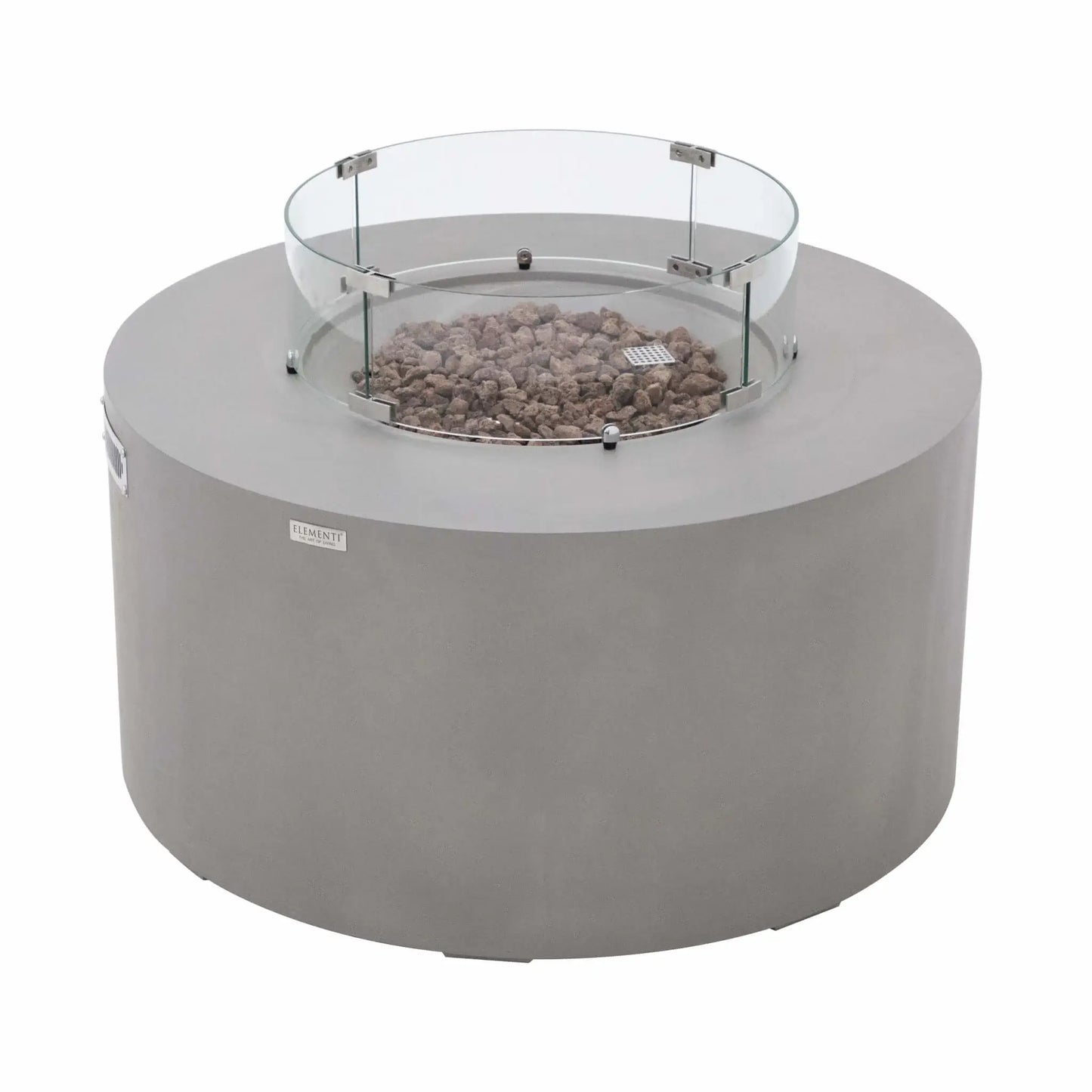 Angled view of the Elementi Art of Living Pacaya round GFRC concrete fire pit table featuring a clear glass wind guard surrounding the lava rock burner area. The image showcases the smooth light grey concrete finish, circular fire bowl design, stainless steel mounting hardware, and contemporary styling that makes the Pacaya fire table a centerpiece for outdoor entertaining spaces.