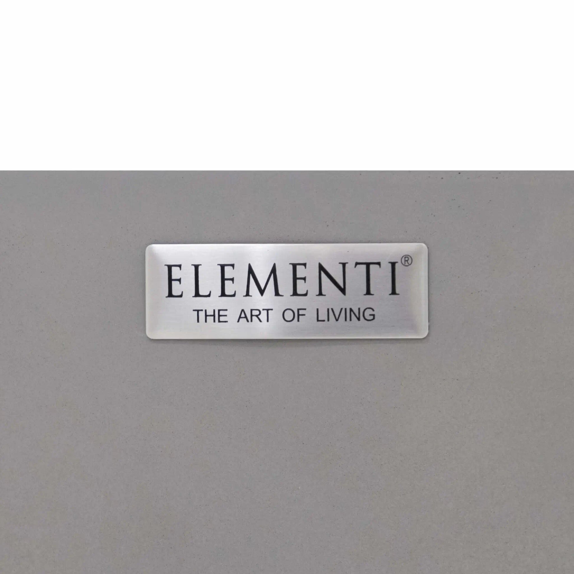 Close-up product detail of the Elementi Art of Living brand badge mounted on the Pacaya Light Grey round GFRC concrete fire pit table. The brushed metal logo plaque features the Elementi The Art of Living branding and highlights the premium craftsmanship, quality materials, and designer finish associated with this modern outdoor fire pit collection.