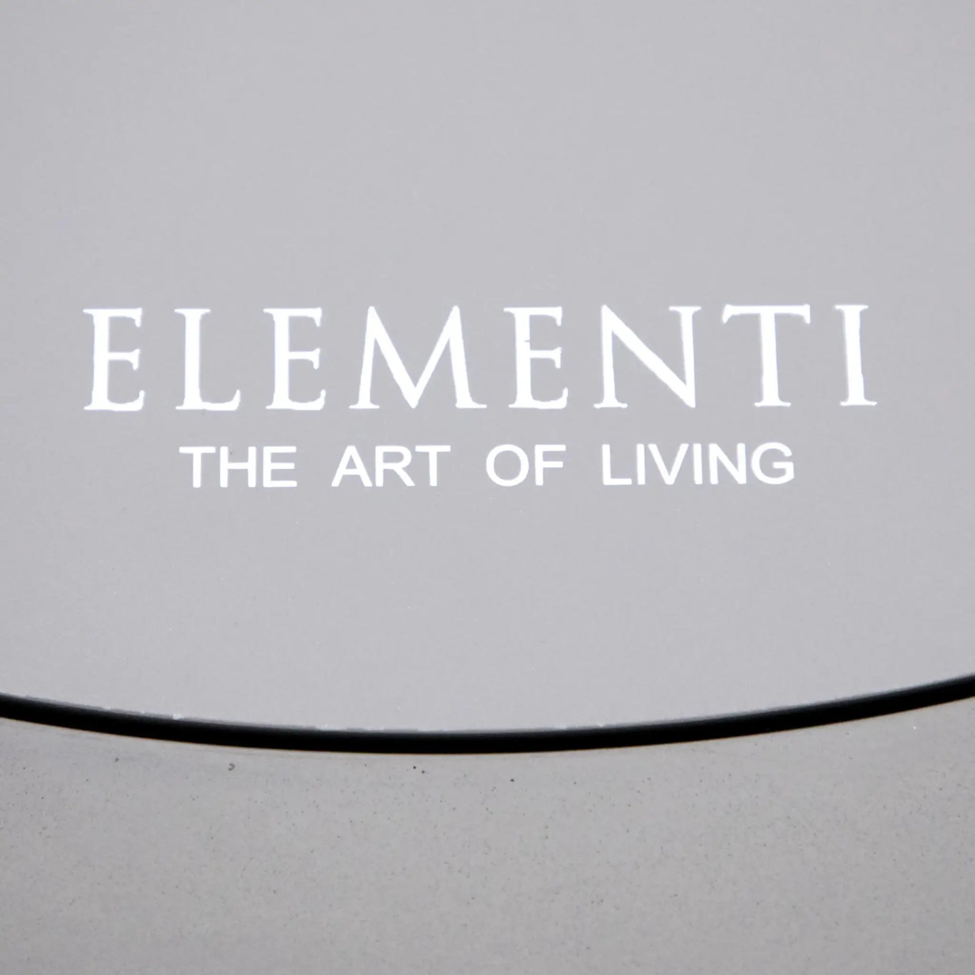 Detailed view of the Elementi The Art of Living logo printed on the circular burner lid of the Pacaya Light Grey GFRC concrete fire pit table. The image emphasizes the branded burner cover, smooth concrete surface, and premium finish that allows the round fire pit table to function as an elegant outdoor coffee table when the burner is covered.