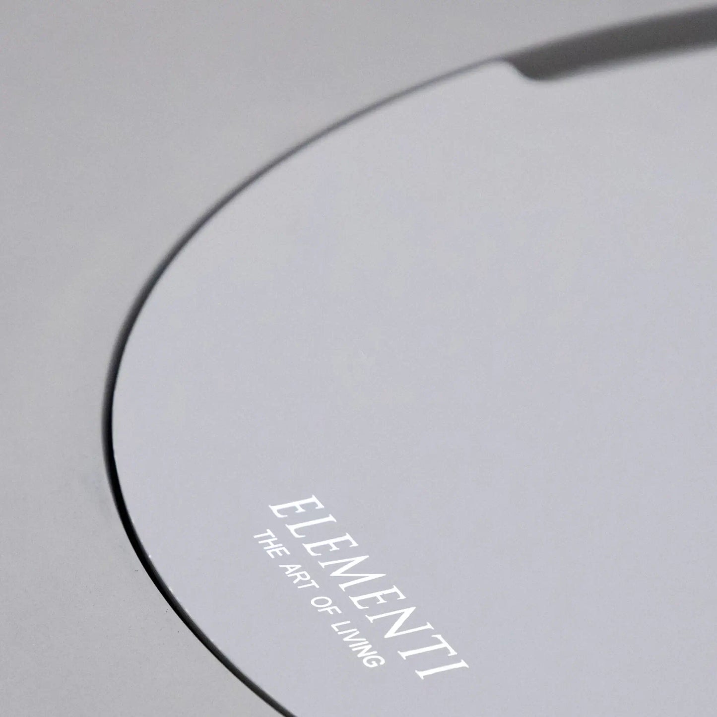 Angled close-up of the Elementi Art of Living branded burner lid installed on the Pacaya Light Grey round GFRC concrete fire pit table. The image showcases the seamless circular cover design, recessed lift handle, and smooth concrete finish, highlighting the hidden burner concept and convertible tabletop functionality of this outdoor propane fire pit.
