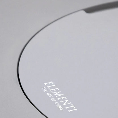 Angled close-up of the Elementi Art of Living branded burner lid installed on the Pacaya Light Grey round GFRC concrete fire pit table. The image showcases the seamless circular cover design, recessed lift handle, and smooth concrete finish, highlighting the hidden burner concept and convertible tabletop functionality of this outdoor propane fire pit.