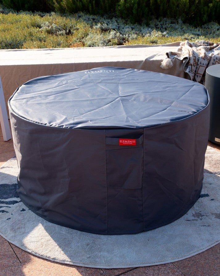 "Elementi Pacaya Round Fire Pit Table fully covered with a durable, weather-resistant protective cover. Designed to shield the dark grey GFRC concrete fire pit from outdoor elements, this fitted cover ensures longevity and year-round protection. Featuring the Elementi logo and a sleek design, it blends seamlessly into any patio or outdoor setting while keeping the fire pit safe and ready for use.