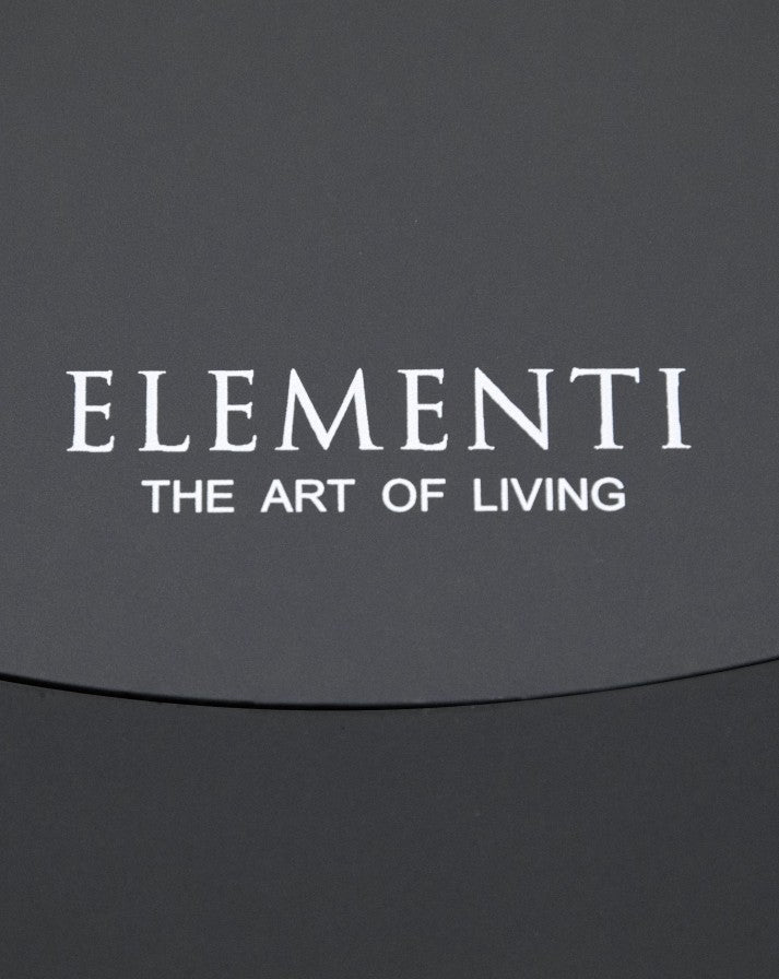 Close-up of the Elementi Pacaya Round Fire Pit Table burner cover, showcasing the brand's signature engraving—'Elementi: The Art of Living.' The sleek, dark grey GFRC concrete finish highlights the fire pit’s premium craftsmanship and minimalist design, reinforcing its modern, high-end aesthetic for luxury outdoor spaces.