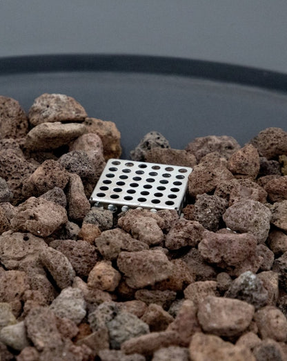 Close-up of the Elementi Pacaya Round Fire Pit Table’s burner system, featuring a stainless steel gas diffuser nestled within natural lava rocks. The porous lava stones enhance heat distribution, while the precision-engineered burner ensures an even, mesmerizing flame for a warm and inviting outdoor ambiance. A perfect blend of functionality and modern fire pit design.