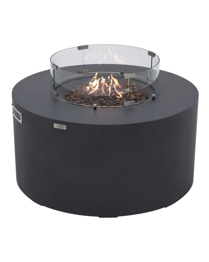 Elementi Pacaya Round Fire Pit Table in dark grey GFRC concrete, showcasing a vibrant flame over natural lava rocks with a sleek tempered glass wind guard. Featuring a hidden propane tank for a seamless design, this modern fire pit enhances outdoor spaces with warmth, ambiance, and wind protection, making it an elegant centerpiece for patios and backyard gatherings.