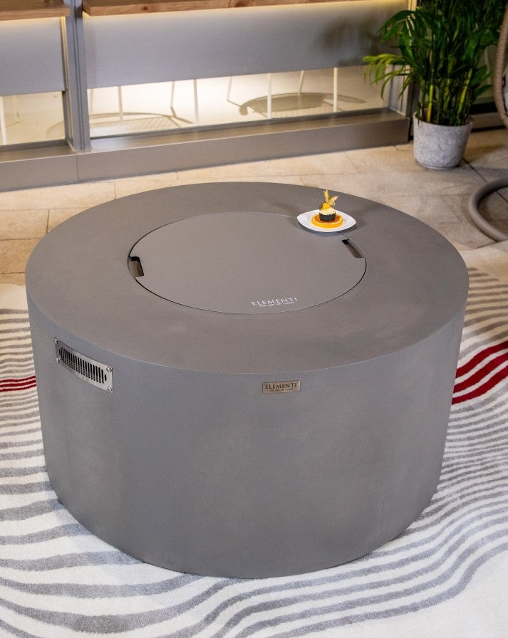 Close-up of the Elementi Pacaya Round Hidden Propane Tank Fire Pit Table in light grey GFRC concrete, featuring a sleek burner cover for a seamless transition from fire pit to functional outdoor coffee table.