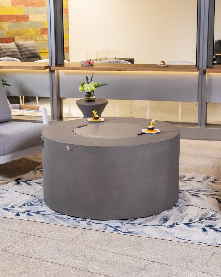 Stylish Elementi Pacaya Round Hidden Propane Tank Fire Pit Table in light grey GFRC concrete, elegantly set in a modern outdoor space with the burner cover on, doubling as a functional coffee table for versatile entertaining.