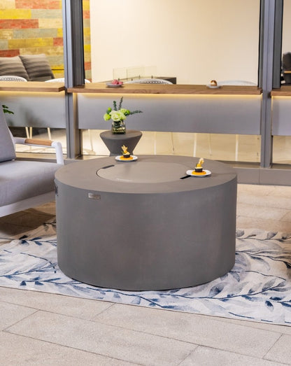 Stylish Elementi Pacaya Round Hidden Propane Tank Fire Pit Table in light grey GFRC concrete, elegantly set in a modern outdoor space with the burner cover on, doubling as a functional coffee table for versatile entertaining.