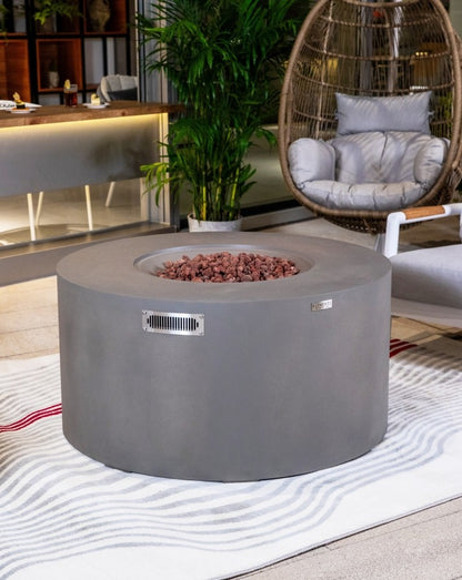 Elementi Pacaya Round Hidden Propane Tank Fire Pit Table in light grey GFRC concrete, elegantly placed in a modern outdoor lounge, featuring natural lava rocks and a sleek ventilation panel for both style and functionality.