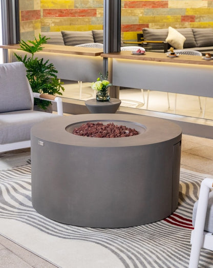 Elementi Pacaya Round Hidden Propane Tank Fire Pit Table in light grey GFRC concrete, elegantly styled in an outdoor lounge setting, featuring natural lava rocks for a warm and inviting ambiance.