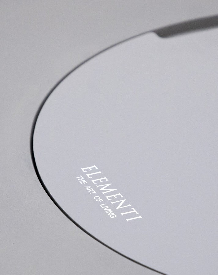 Close-up of the Elementi Pacaya Round Fire Pit Table’s burner cover, featuring a sleek light grey GFRC concrete finish with the 'Elementi - The Art of Living' branding, highlighting its modern and sophisticated design.