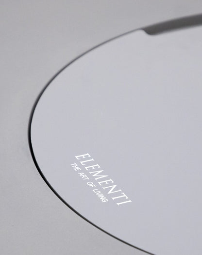Close-up of the Elementi Pacaya Round Fire Pit Table’s burner cover, featuring a sleek light grey GFRC concrete finish with the 'Elementi - The Art of Living' branding, highlighting its modern and sophisticated design.