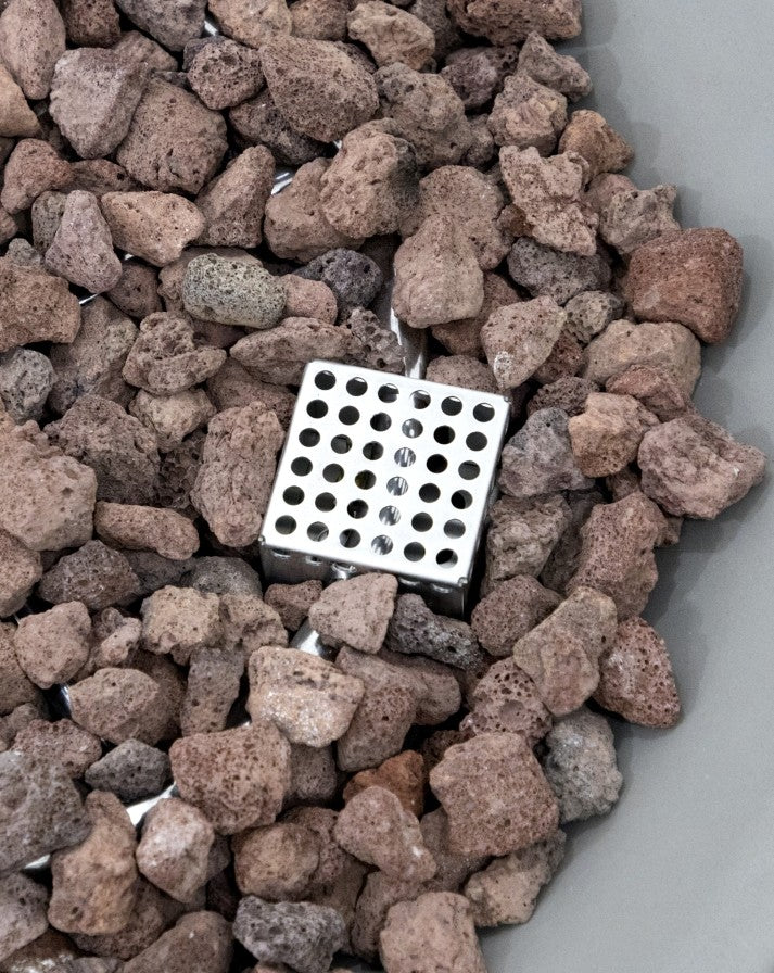 Detailed close-up of the Elementi Pacaya Round Hidden Propane Tank Fire Pit Table showcasing its precision-engineered stainless steel burner surrounded by natural lava rocks. This modern GFRC concrete fire pit offers durability, efficient heat distribution, and a contemporary aesthetic for outdoor living spaces.