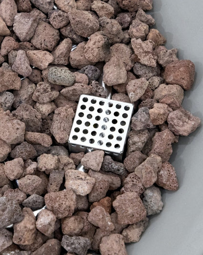 Detailed close-up of the Elementi Pacaya Round Hidden Propane Tank Fire Pit Table showcasing its precision-engineered stainless steel burner surrounded by natural lava rocks. This modern GFRC concrete fire pit offers durability, efficient heat distribution, and a contemporary aesthetic for outdoor living spaces.